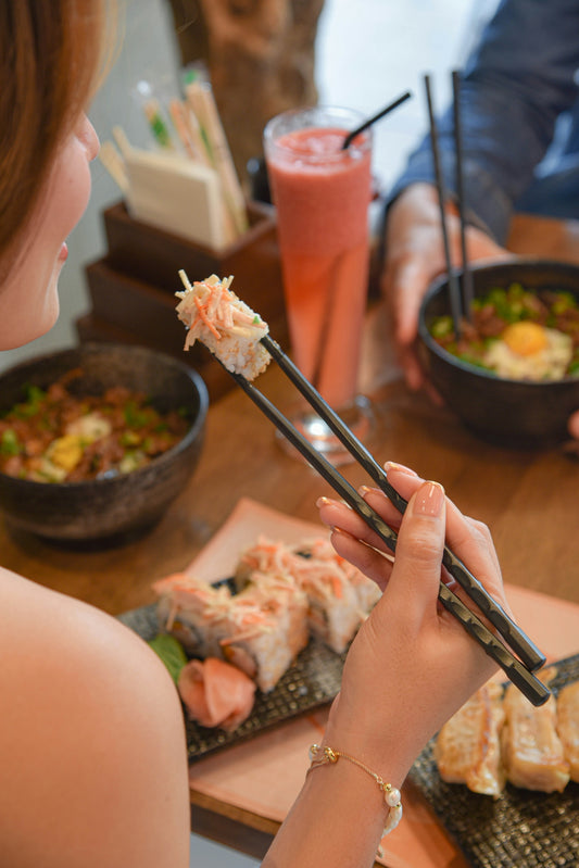 a woman eating sushi with chopsticks at a table