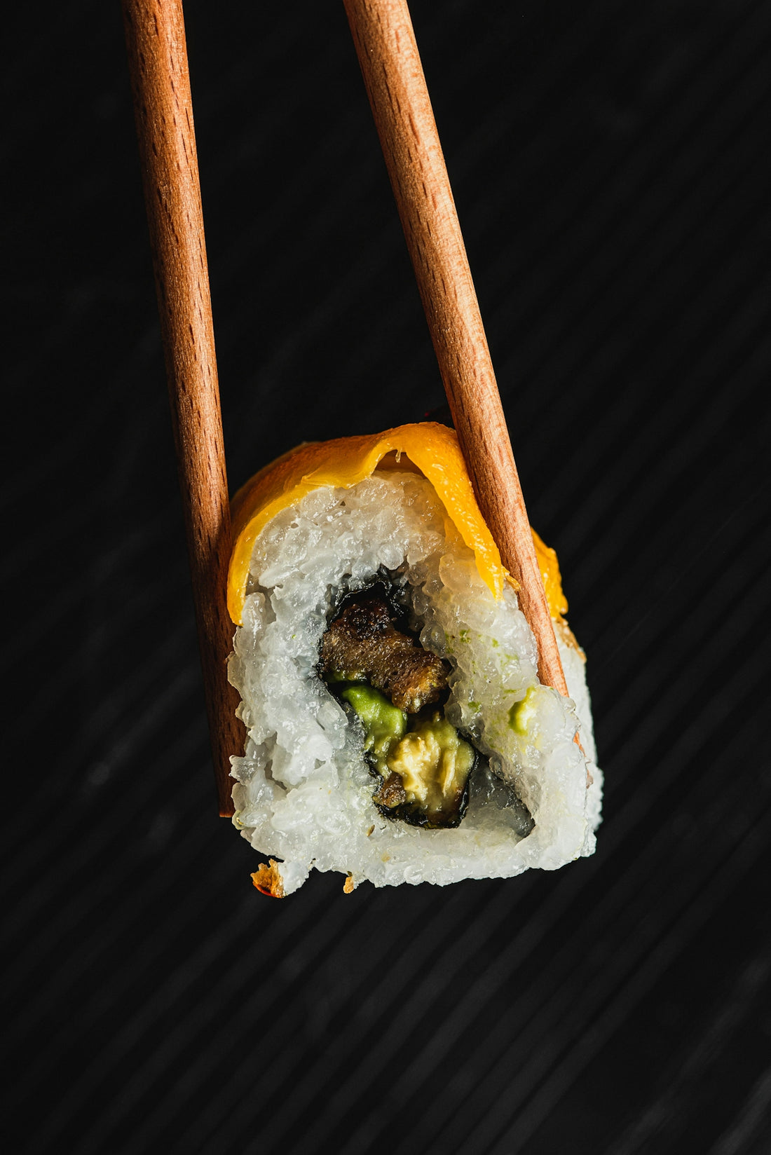 Chopsticks holding a sushi roll with avocado and eel.