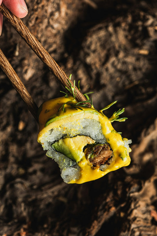 Chopsticks holding a sushi roll with avocado and sauce.
