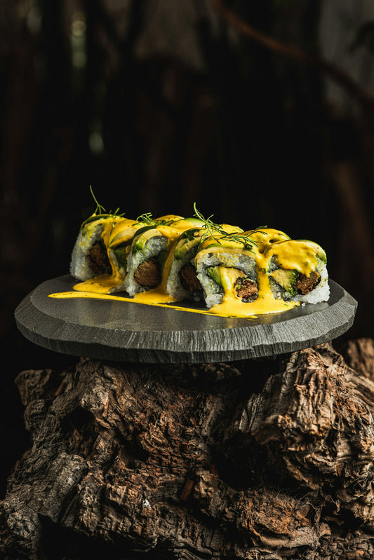 Sushi rolls drizzled with yellow sauce on a dark plate.